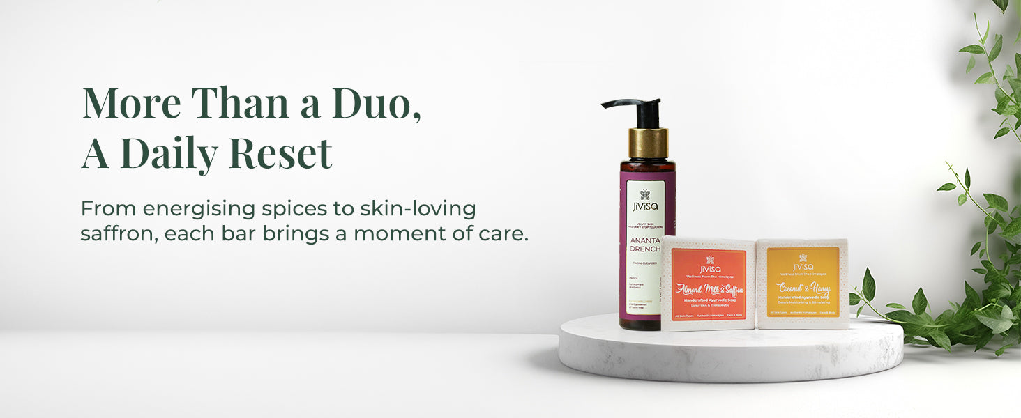 JiViSa Ananta Drench Cleanser with Coconut & Honey and Almond Milk & Saffron Ayurvedic Soap Bars placed on a white marble pedestal surrounded by green leaves. Text on the left reads: “More Than a Duo, A Daily Reset.” Subtext: “From energising spices to skin-loving saffron, each bar brings a moment of care.”

