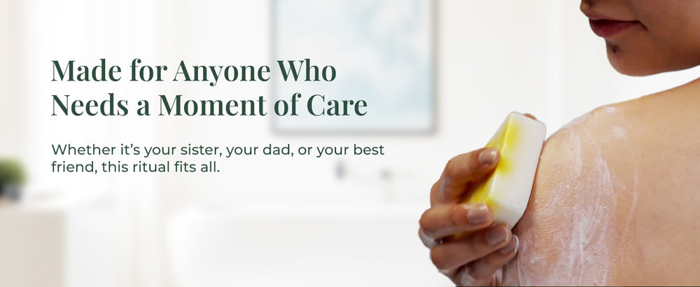 A woman using the JiViSa Coconut & Honey Ayurvedic Soap on her shoulder, creating a soft lather. Text on the left reads: “Made for Anyone Who Needs a Moment of Care.” Subtext: “Whether it’s your sister, your dad, or your best friend, this ritual fits all.”

