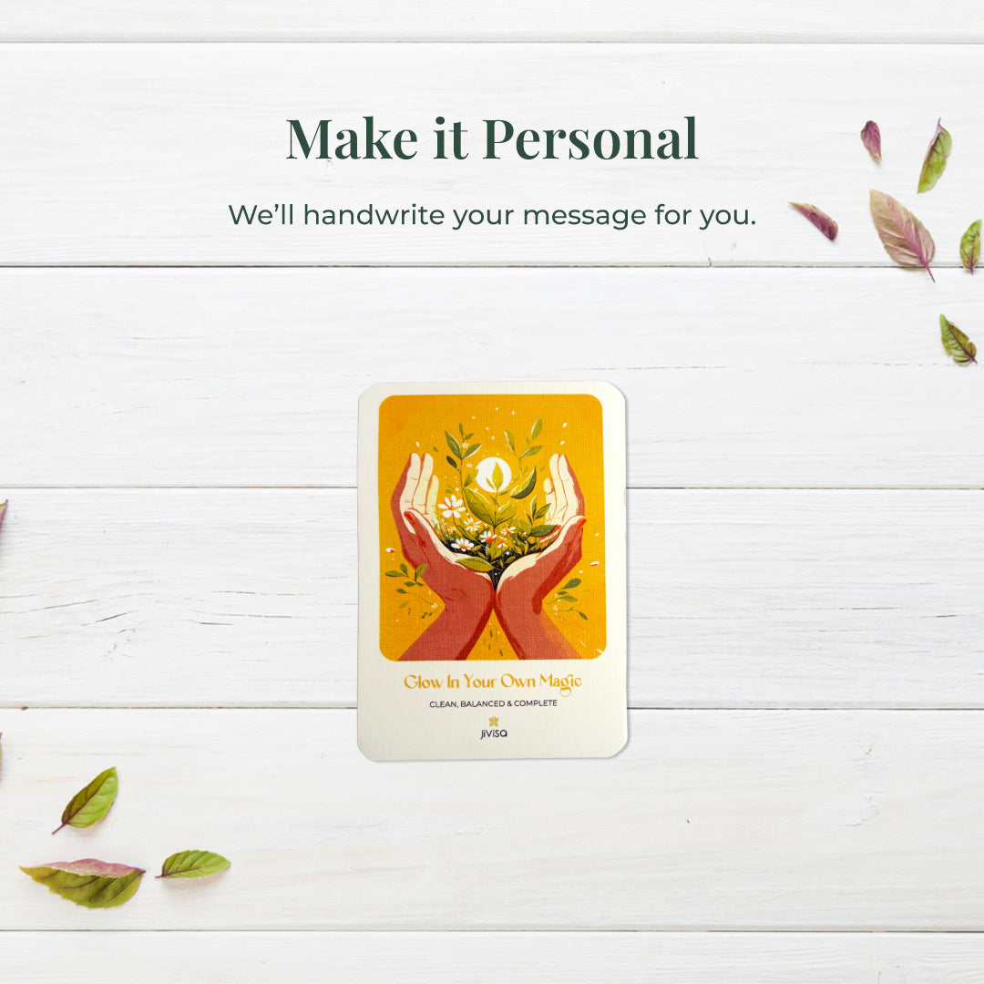 &quot;Make it personal – We’ll handwrite your message for you.&quot; A handwritten card with warm yellow and orange tones shows two hands holding blooming herbs with a glowing sun. Placed on a white surface, the image emphasizes the personal, heartfelt gifting experience JiViSa offers.
