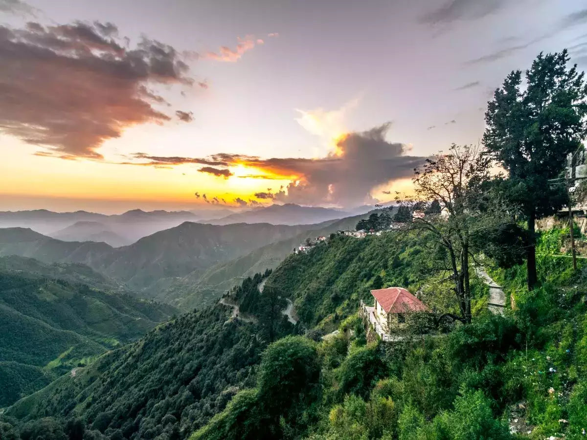 A peaceful sunset over the Himalayan mountains with lush green valleys and a quiet hillside home, reflecting JiViSa’s roots in nature inspired wellness Ayurveda purity and slow living philosophy.