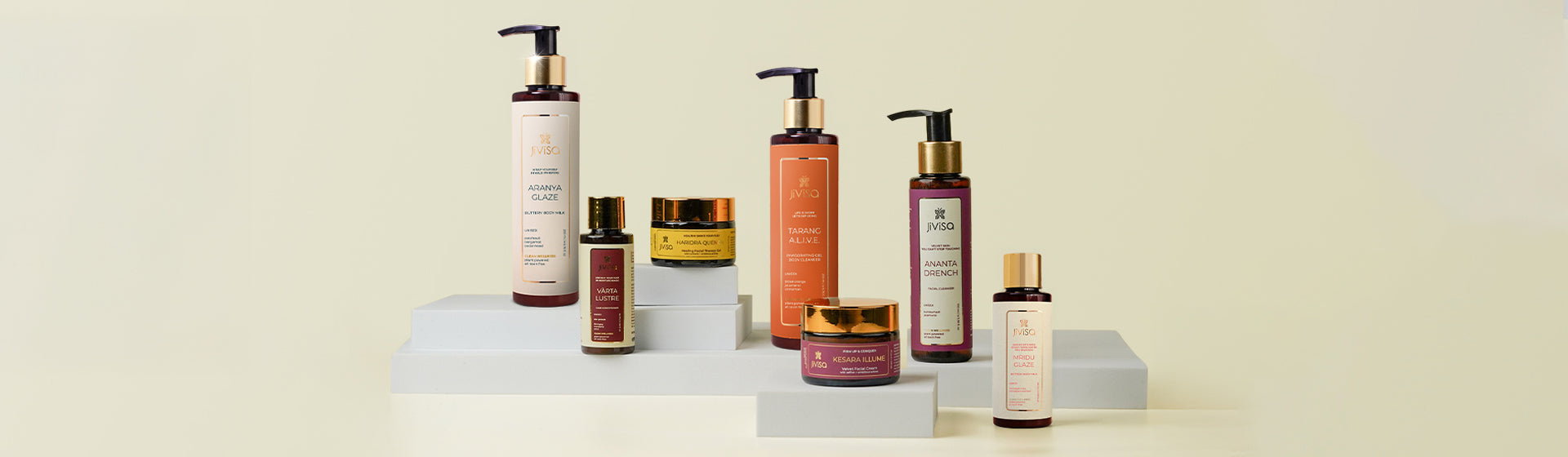 JiViSa’s clean skincare collection displayed on minimalist platform, featuring Aranya Glaze Nourishing Body Milk, Varta Lustre Hair Conditioner, Tarang A.L.I.V.E Rejuvenating Body Wash, Haridra Quench Healing Facial Therapy Gel, Kesara Illume Radiance Moisturiser, Ananta Drench Facial Cleanser, and Mridu Glaze Hydrating Body Milk—crafted to deeply nourish, brighten, and rejuvenate skin.. The elegant packaging in gold and earthy tones reflects JiViSa’s luxurious yet natural approach to skincare and wellness.