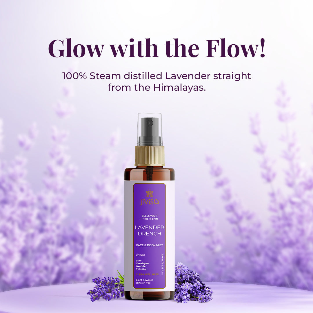 A bottle of JiViSa Lavender Drench Face & Body Mist placed on a lavender-themed background with fresh lavender flowers. The label highlights it as a unisex, plant-powered, toxin-free mist made from 100% steam-distilled lavender from the Himalayas. Text above reads 'Glow with the Flow!' and emphasizes the product's natural origin.