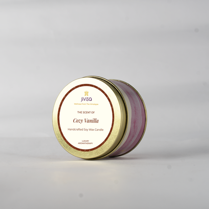 JiViSa Cozy Vanilla handcrafted soy wax candle in a closed gold tin with a decorative pink and white swirl pattern, seen from a slight angle on a plain white background. The label reads: &quot;JiViSa Wellness From The Himalayas, THE SCENT OF Cozy Vanilla, Handcrafted Soy Wax Candle, LUXURY AROMATHERAPY&quot;.